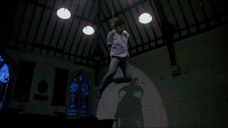 One of the victims hangs from the ceiling as the killer is shown in silhouette in Slaughter High (1986).