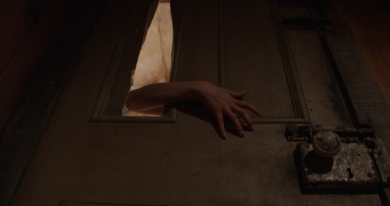 Lorraine (Jenna Ortega) reaching through a door in X (2022).