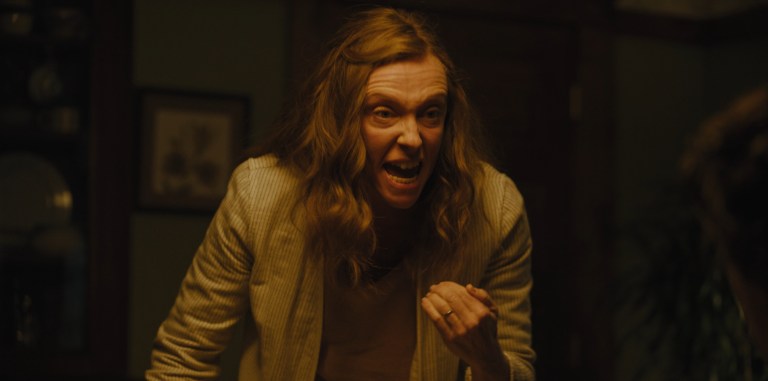 Toni Collette yells during dinner in Hereditary (2018).