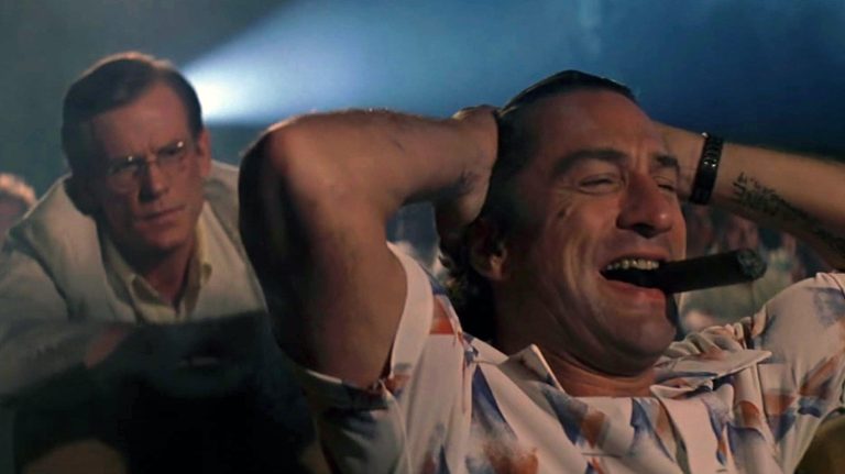 Robert De Niro as Max Cady laughs and smokes in a movie theater in Cape Fear (1991).