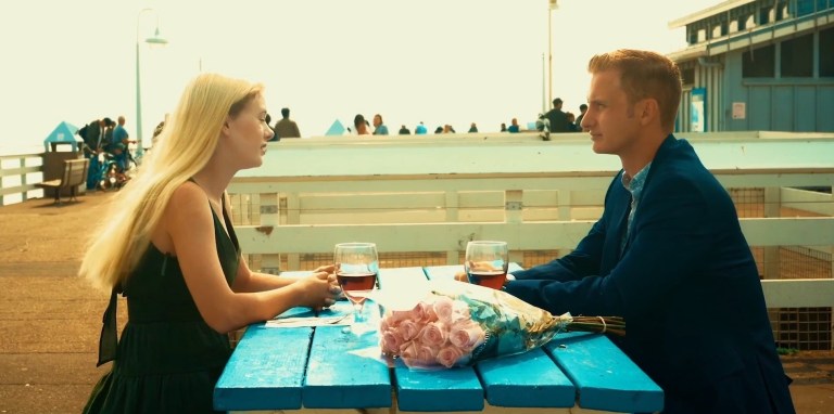 Kim and Evan sit at a bench on a pier in Birdemic 3: Sea Eagle (2022).