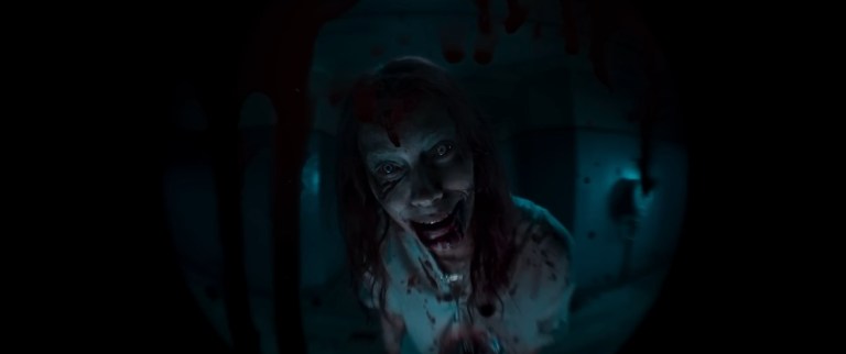 The Deadite Ellie smiles as she looks through a peephole in Evil Dead Rise (2023).