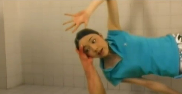 A woman is grabbed by the head by an arm reaching out of a shower drain in The Groaning Drain (2004).