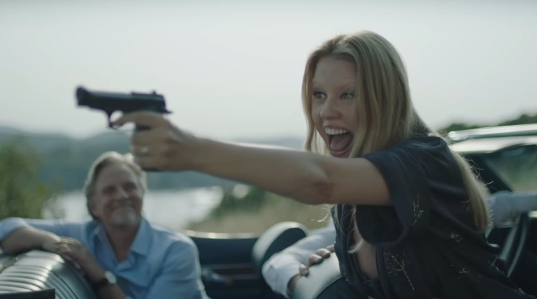 Mia Goth (Gabi) smiles as she points a gun at James in Infinity Pool (2023).