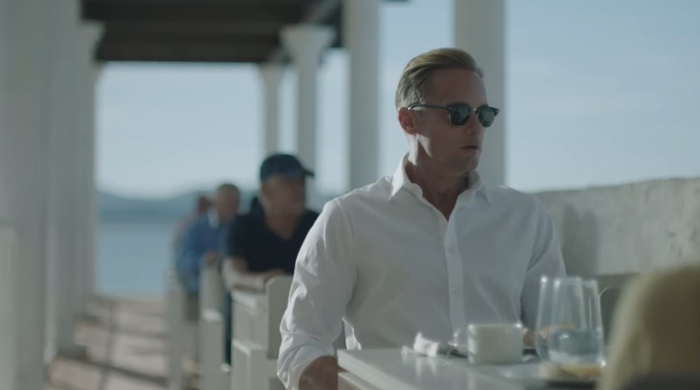 Alexander Skarsgård sitting at a table outside in Infinity Pool (2023).