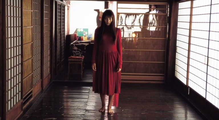 A woman in a red dress stares forward in a Japanese room in Kakashi (2001).