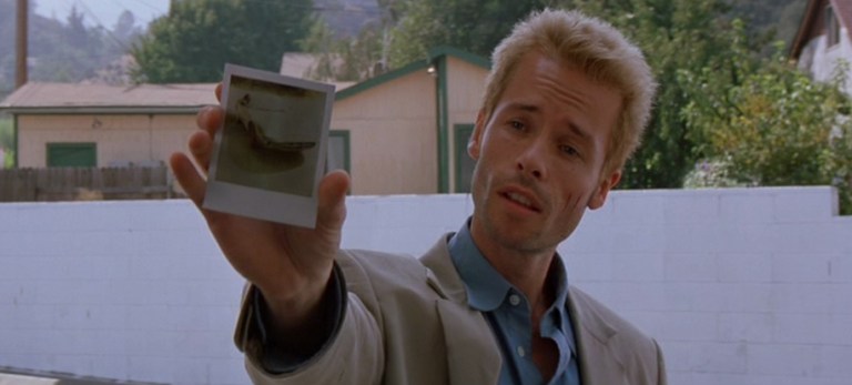 Guy Pearce hold out a Polaroid photograph in Memento (2000).