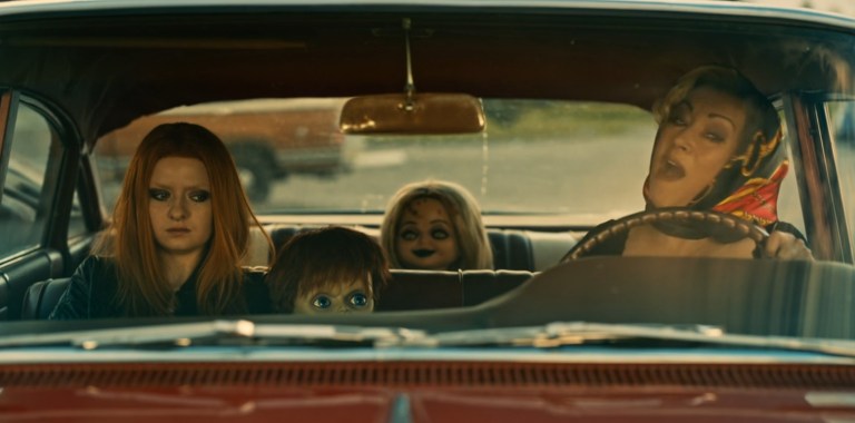 Tiffany freaks out behind the wheel of a car as Glen, Glenda, and Jennifer Tilly in a doll sit as passengers.