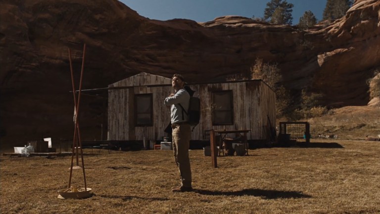 Wyndham looks around while standing in front of a rundown house in The Seeding (2023).