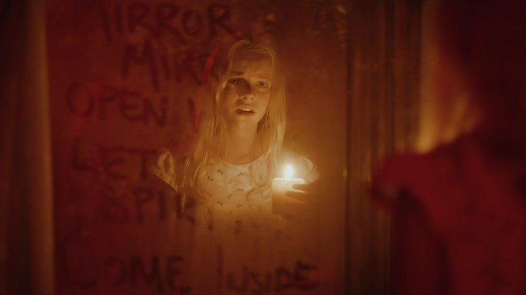Elizabeth Birkner holds a candle while looking into a mirror in Behind You (2020).