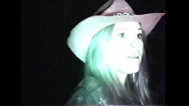 Amy, wearing a cowboy hat, looks frightened in the dark in Frogman (2024).