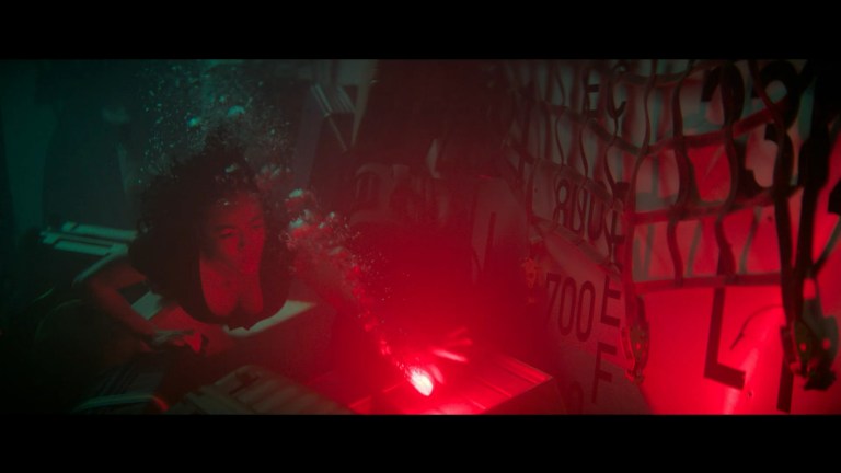 Ava swims through the baggage hold of a submerged airplane in No Way Up (2024).