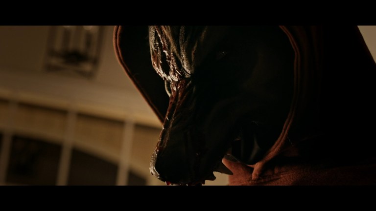 A person in a wolf mask, wearing a red hooded sweatshirt in Prey for the Bride (2024).