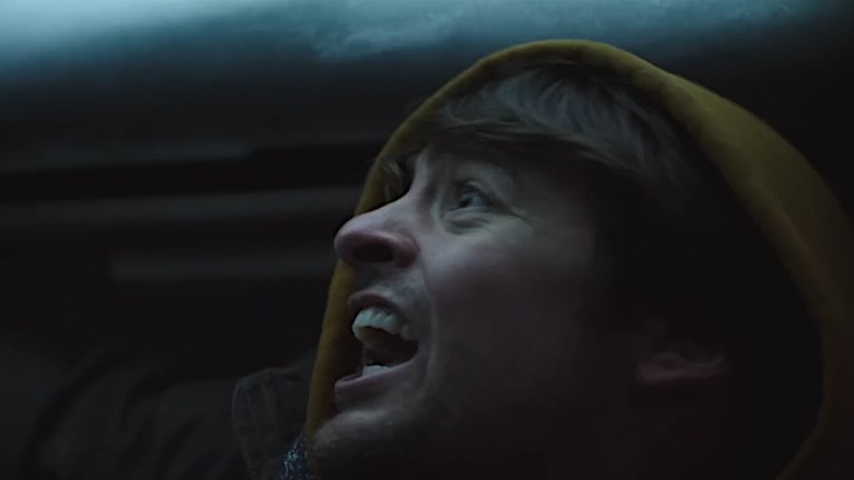 A man yells while looking up at the snow-covered sunroof of his car in Centigrade (2020).