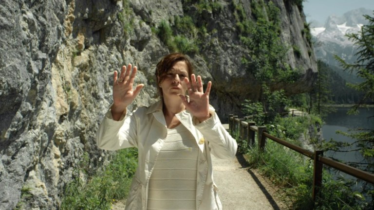 A woman places her hands on an invisible wall inexplicably standing in front of her on a path in the mountains in The Wall (2012).