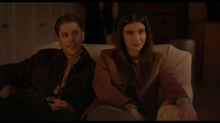 Aleks and Anna Smile while sitting together on a couch in All You Need is Death (2023).