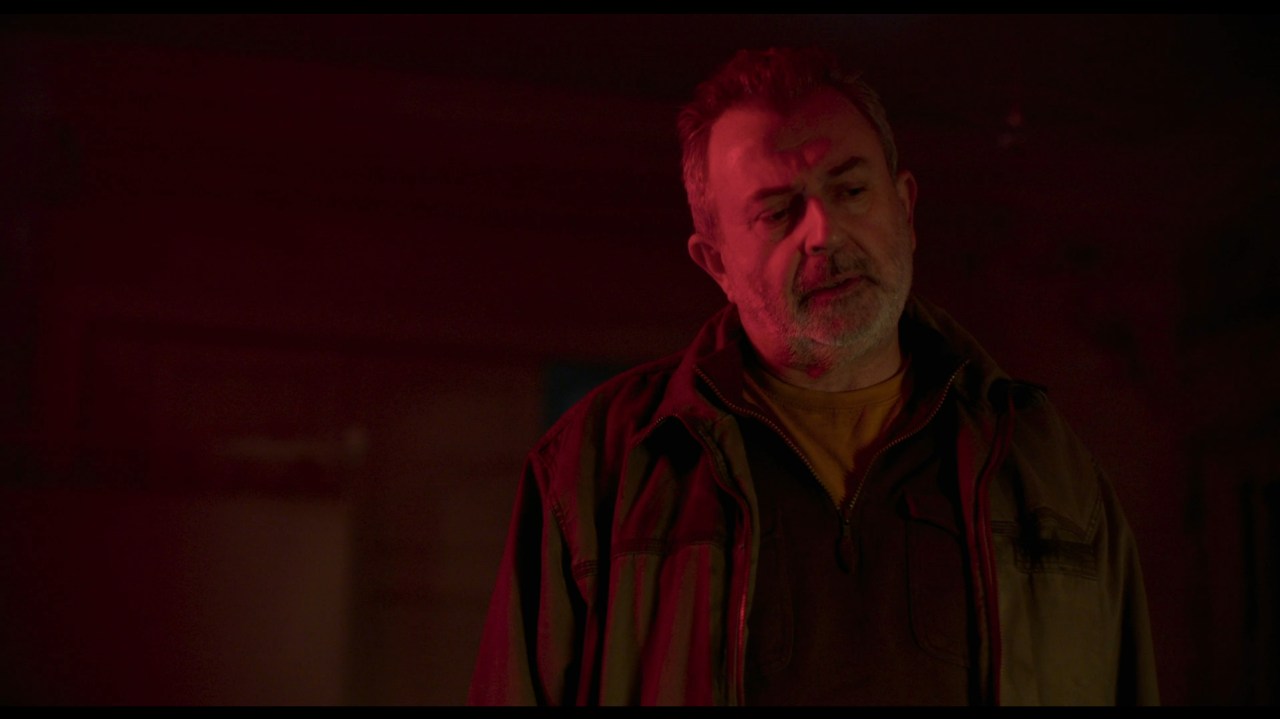 Breezeblock standing in a red light in All You Need is Death (2023).