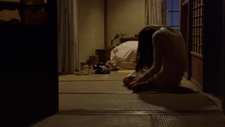 Asami patiently waits in her room for a phone call while an ominous bag lies in the background in Audition (1999).