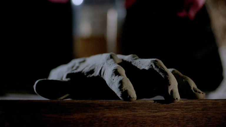 A mummified hand rest on the edge of a table, ready to pounce in Demonoid (1981).