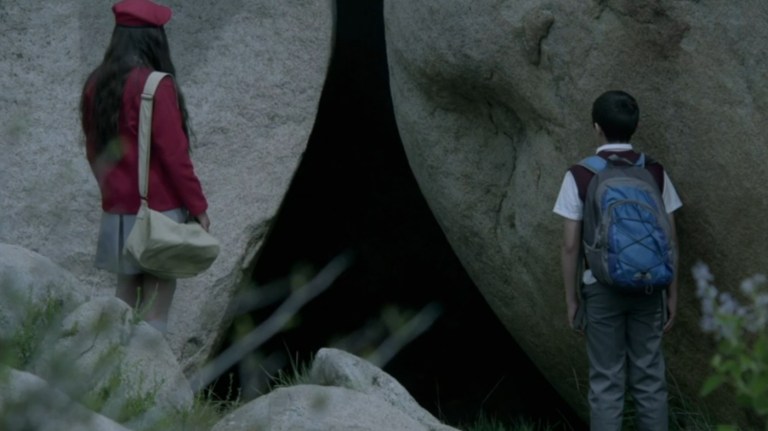 A girl and boy look into an opening between two large rocks in Here Comes the Devil (2012).