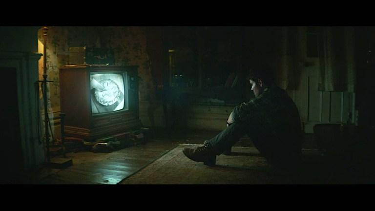 Ron watches TV alone at night in History of Evil (2024).