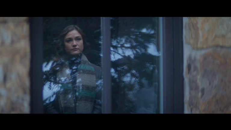 Laura stares out of a window that is reflecting a tree in Snow Valley (2024).