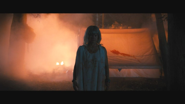 The camp host stands in front of a bloody tent in The Camp Host (2024).