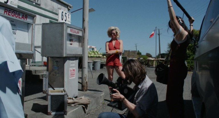 Bobby-Lynne watches as RJ shoots a scene at a gas station in X (2022).