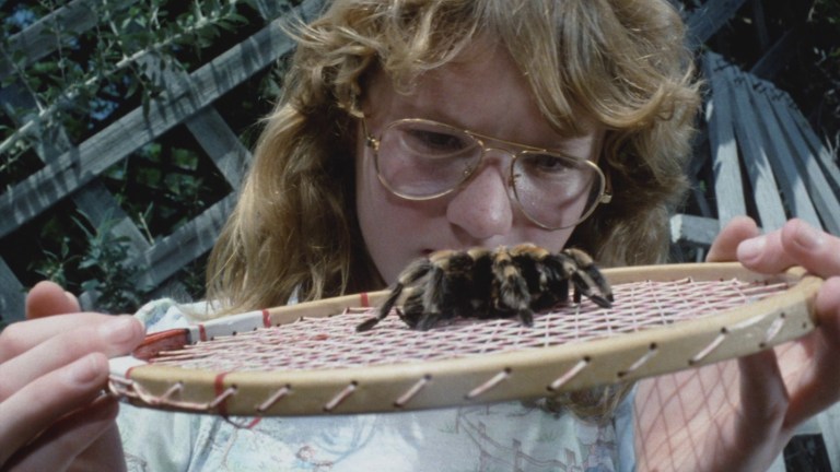 A girl looks at a tarantula on a tennis racket in Tarantulas: The Deadly Cargo (1977).