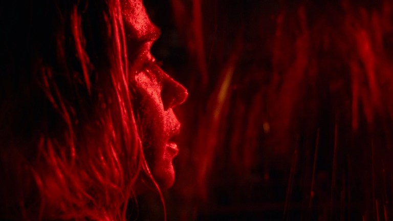 Evelyn is illuminated with red light while she stands behind falling water in A Quiet Place (2018).