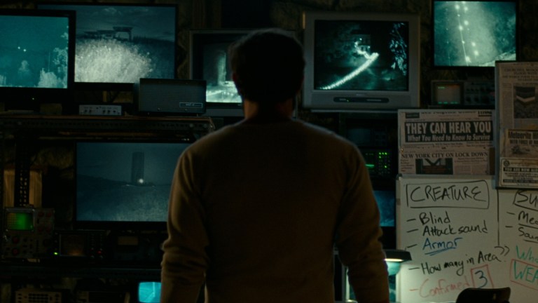 Lee stands in front of a wall of monitors in A Quiet Place (2018).