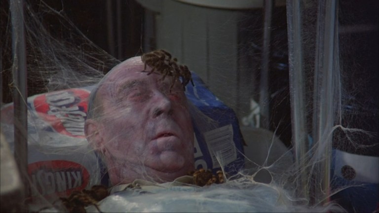 Tarantulas crawl over a man covered in webs in Kingdom of the Spiders (1977).
