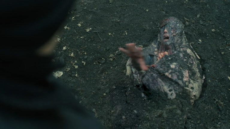 A partially buried man covered in organic material reaches for help in Hell Hole (2024).