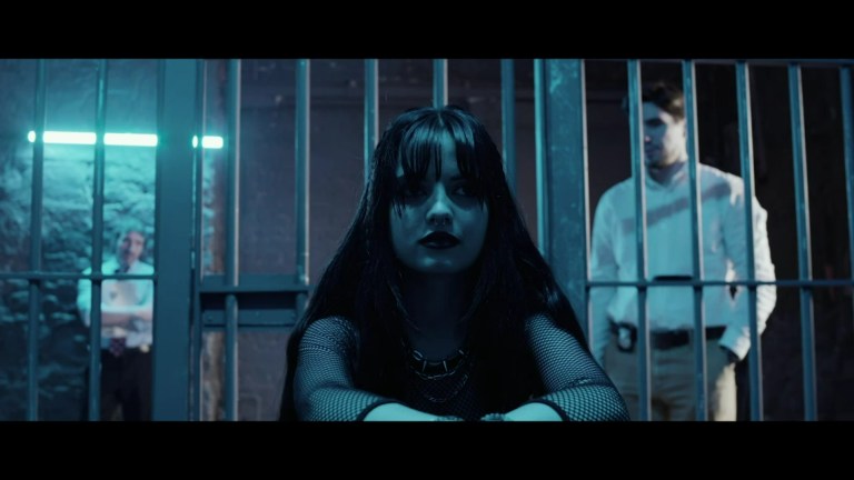 Police stand behind Rebecca and look at her through the bars of a jail cell in The Mouse Trap (2024).