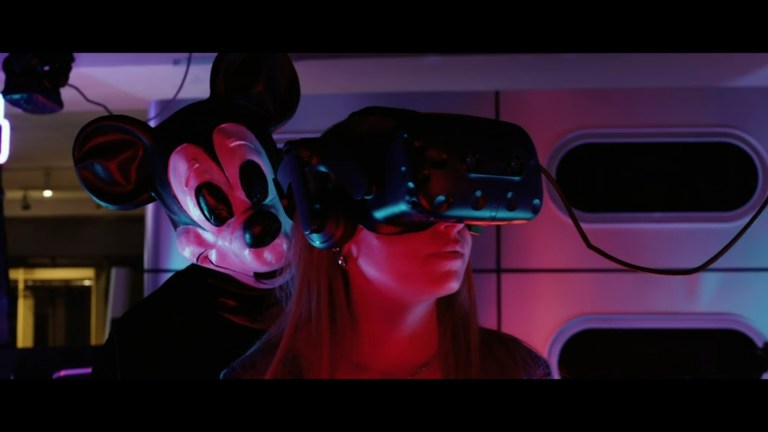 Mickey appears behind Gemma as she uses a VR headset in The Mouse Trap (2024).