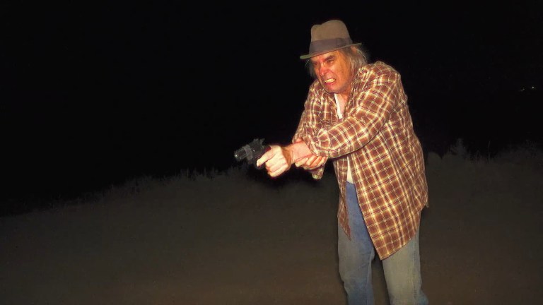 Greg holds a gun in Milk & Serial (2024).