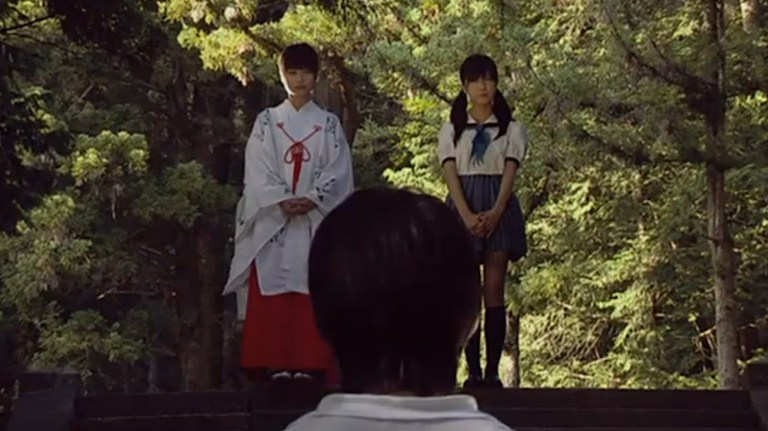 A still image of a boy looking up towards two girls.