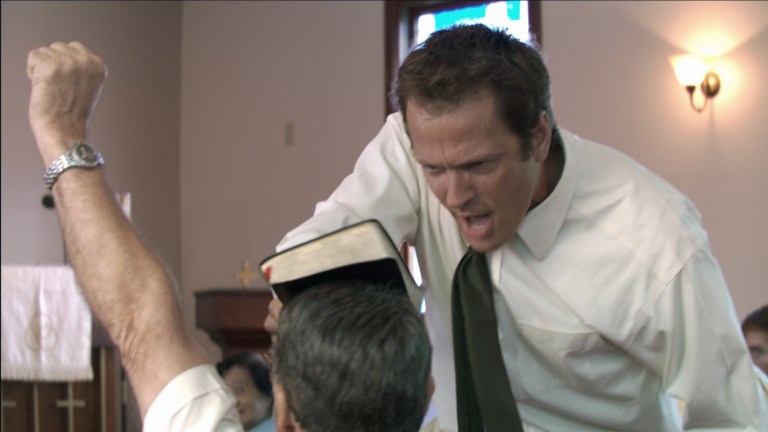 Reverend Cotton Marcus touches a Bible to a man's head in The Last Exorcism (2010).