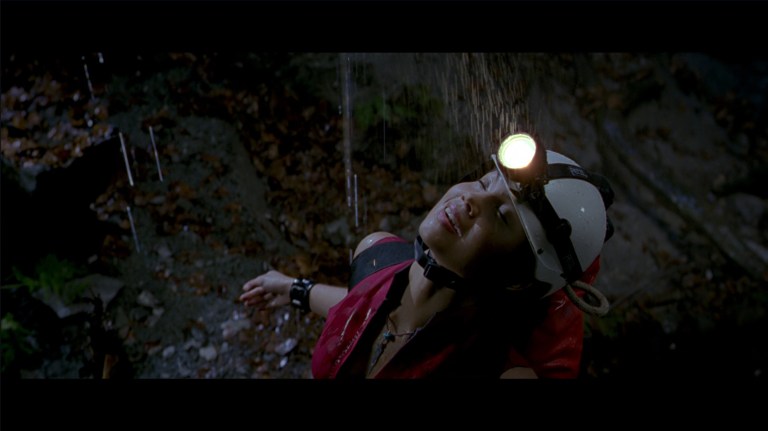 Juno smiles as she feels the water from above drip down in her in The Descent (2005).