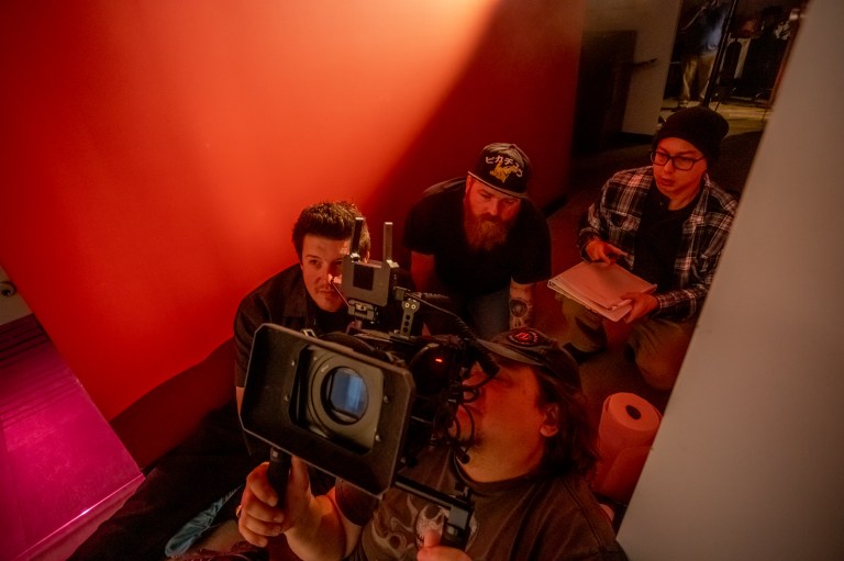 A behind the scenes photo of P.J. Starks with a cameraman and other crew members crouched in a hallway.