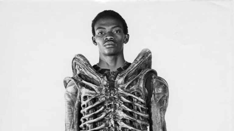 Bolaji Badejo posing in a Xenomorph costume.