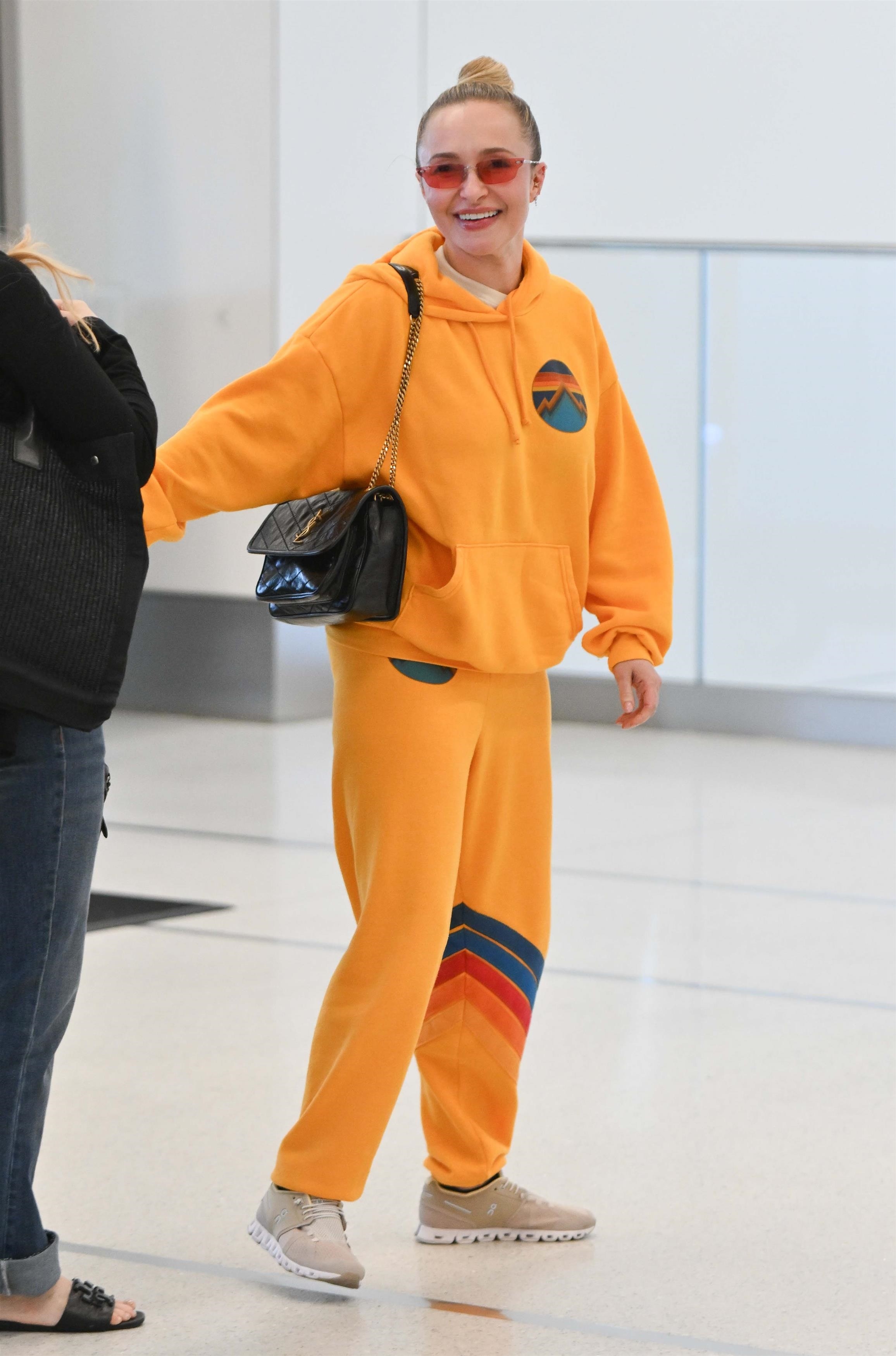 Hayden Panettiere in an orange Aviator Nation hoodie and matching sweatpants walking through LaGuardia Airport