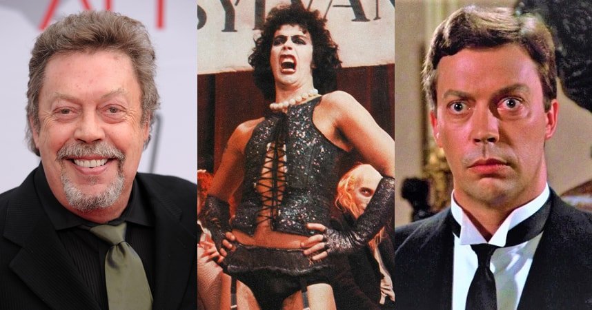Tim Curry smiling on a red carpet, wearing a black suit and olive-green tie, with gray-streaked hair and a goatee.