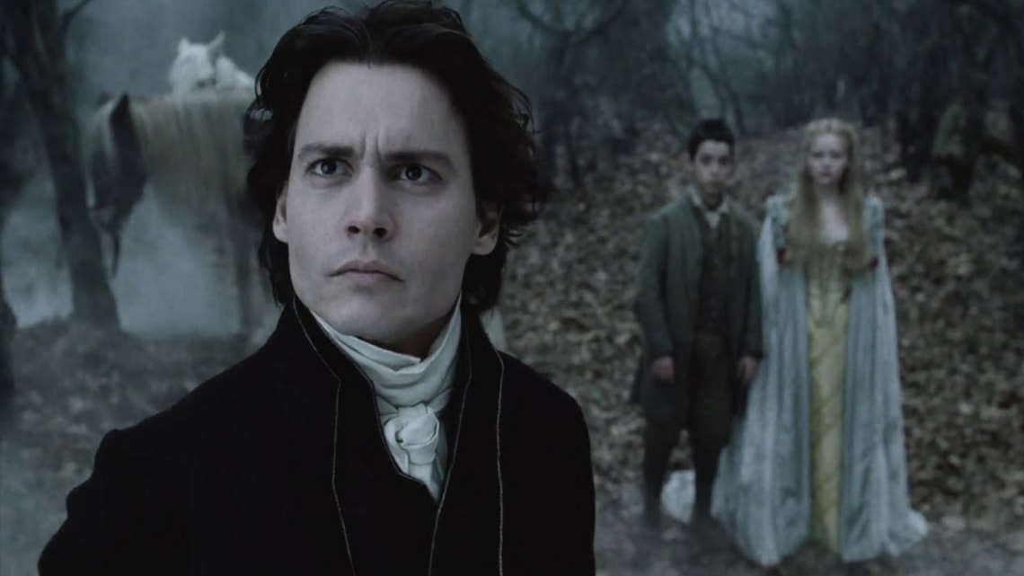 A man in a black period coat stands in a dark foggy forest, with a young man and woman in pale costume and a white horse visible in the background.