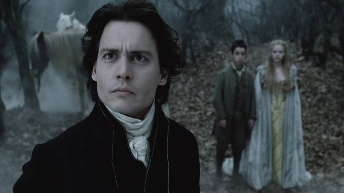 A man in a black period coat stands in a dark foggy forest, with a young man and woman in pale costume and a white horse visible in the background.