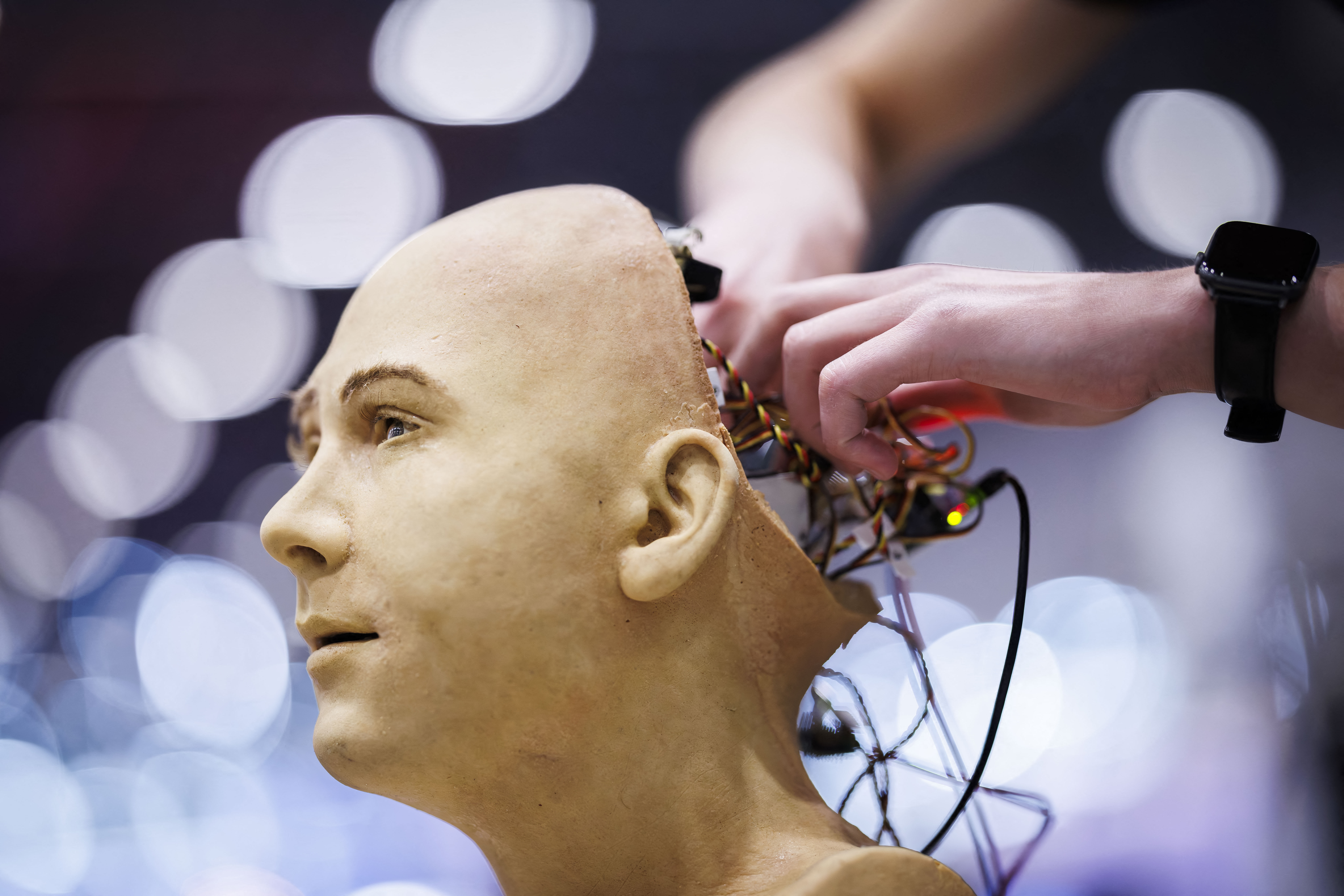 A man working on the internal electronics of Jules, a humanoid AI robot by Hanson Robotics, at a summit stand in Geneva