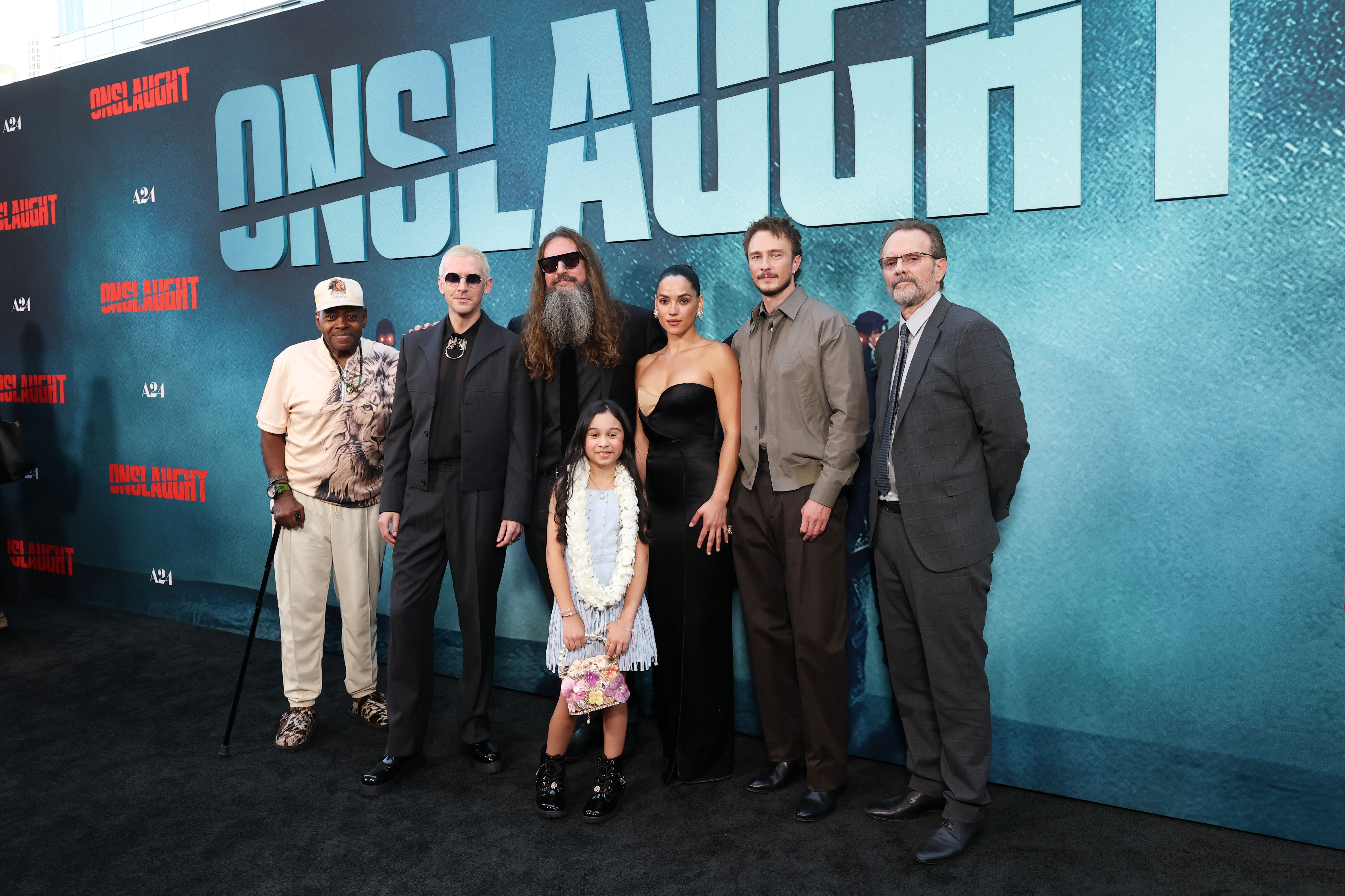 Reginald VelJohnson, Dan Stevens, Adam Wingard, Blake Kennedy, Adria Arjona, Drew Starkey, and Michael Biehn posing together at the A24 Onslaught premiere.