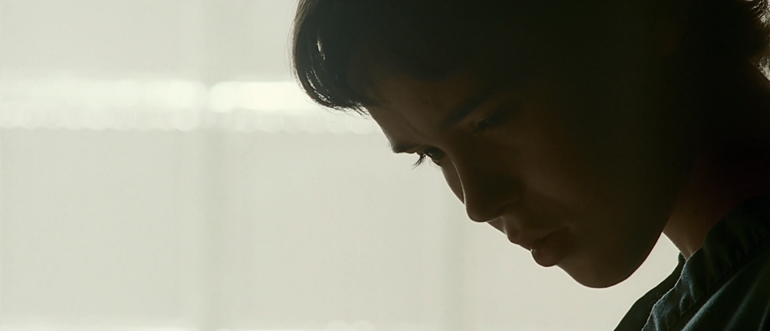 Side profile of a dark-haired person with head bowed, heavily backlit against a bright diffuse background.