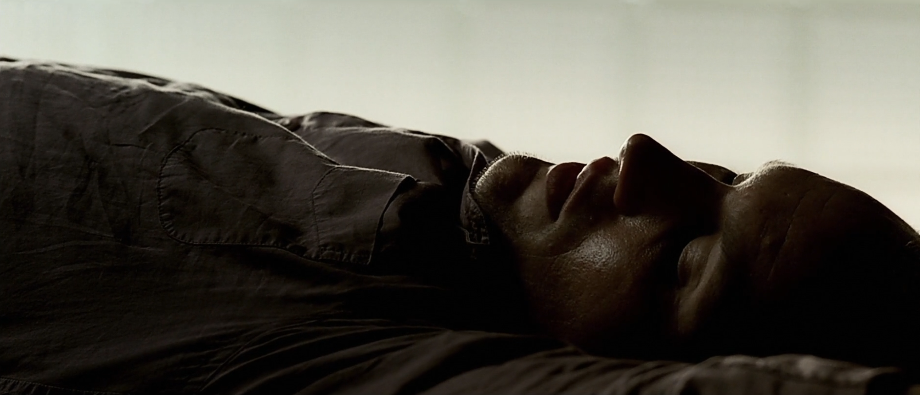 Man in dark clothing lying on his back, face tilted upward, shot in low-key cinematic lighting.