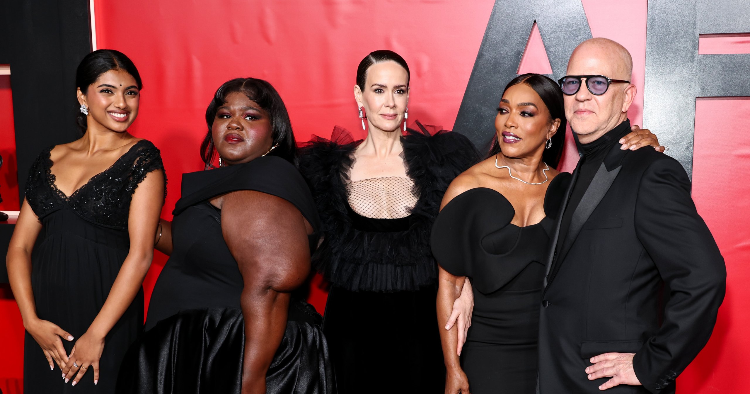 Five cast and crew members of AHS: 13 pose together in black outfits at a red-backdrop premiere event.